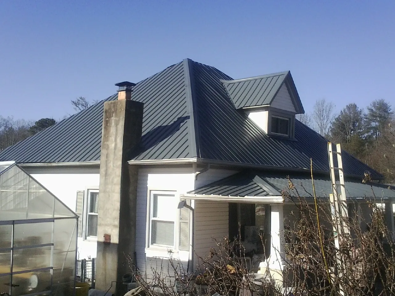 Dark blue standing seam metal roof on a white farmhouse with dormer — Slate & Tile Roof Repair by Roofing Brothers in La Rose
