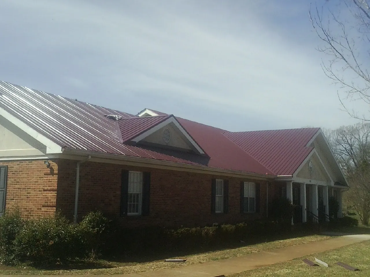 Red metal roof with gabled entries on a long brick building, from a Hail Damage Roof Repair job in La Rose
