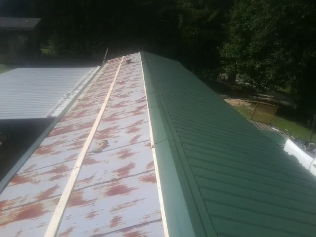 Old rusted panels beside newly installed green metal roofing — Wind Damage Roof Repair by Roofing Brothers in La Rose