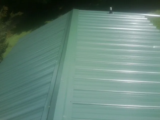New green metal panels meeting at the ridge of a roof — Flat Roof Repair work by our crew in La Rose