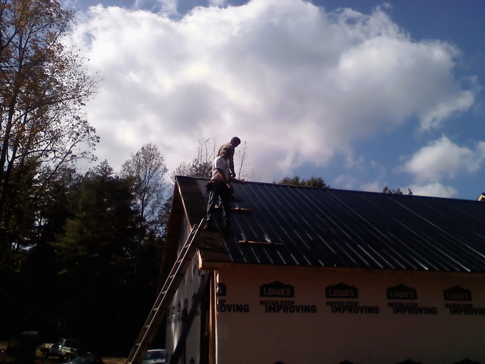 Roofer fastening dark metal panels high against a cloudy sky, from a Roof Inspection job in La Rose