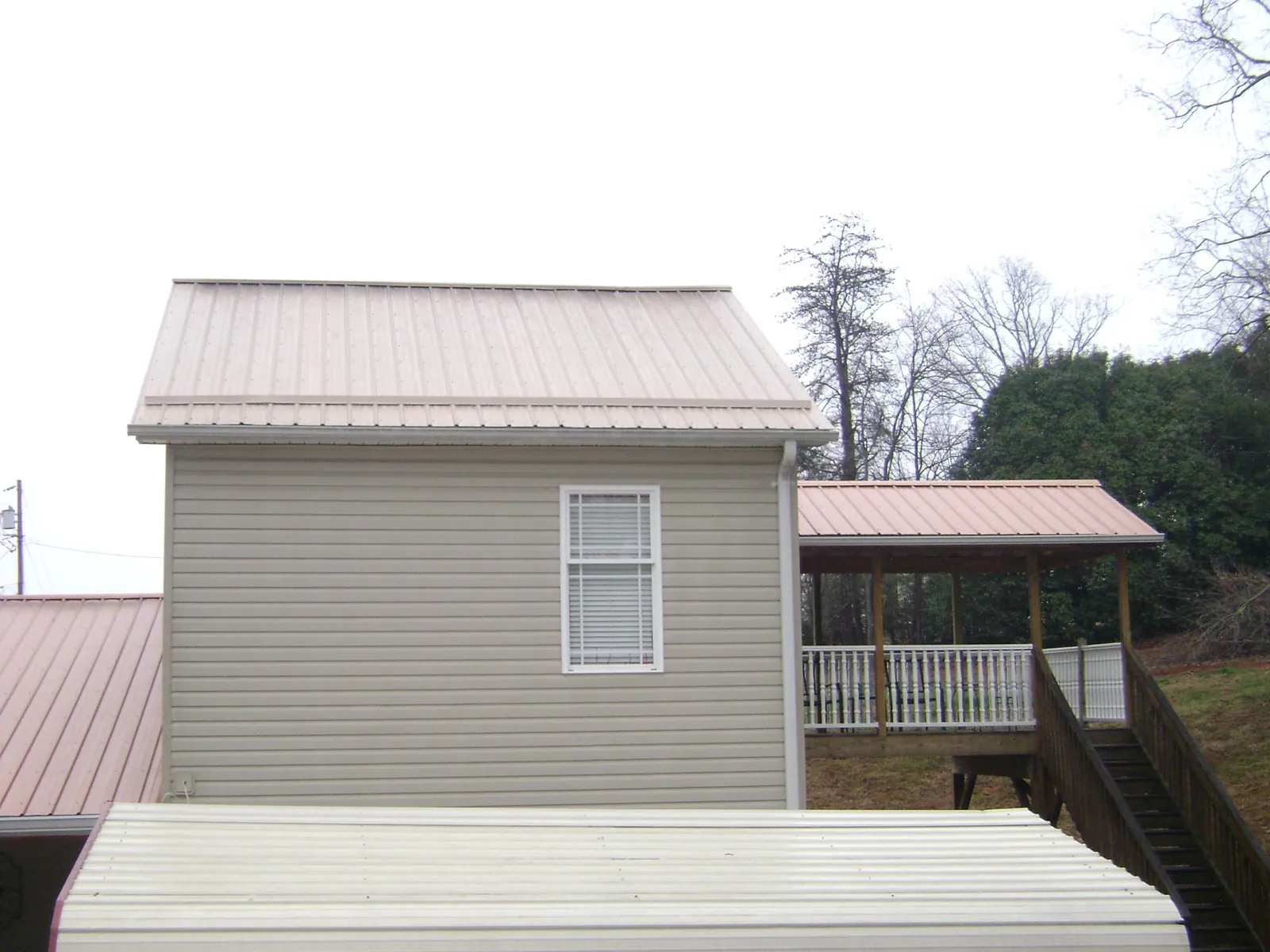 Tan metal roofs on a two story addition and attached porch, from a Roof Replacement job in La Rose